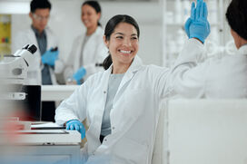 A team of happy scientists in lab coats celebrate with high fives in a bright, modern laboratory. This image captures collaboration, teamwork and scientific breakthroughs—perfect for showcasing a positive research environment.