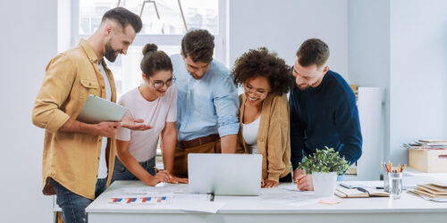 Group of professionals collaborating around a laptop and reviewing charts in a bright office