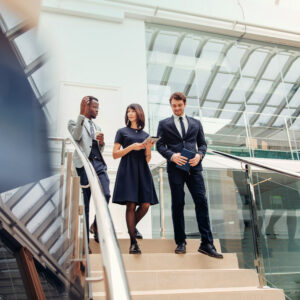 Three professionally dressed individuals walking down a staircase in a modern government or corporate building while conversing