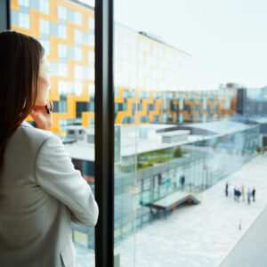 Professional in business attire looking out a large window at a modern government or institutional complex
