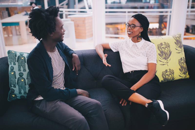 Two businesspeople on a couch, holding a discussion.