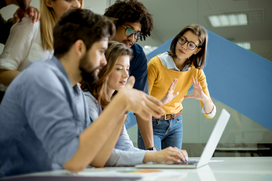 A group of professionals gathered around a laptop in a modern office, discussing workforce strategy and solutions.