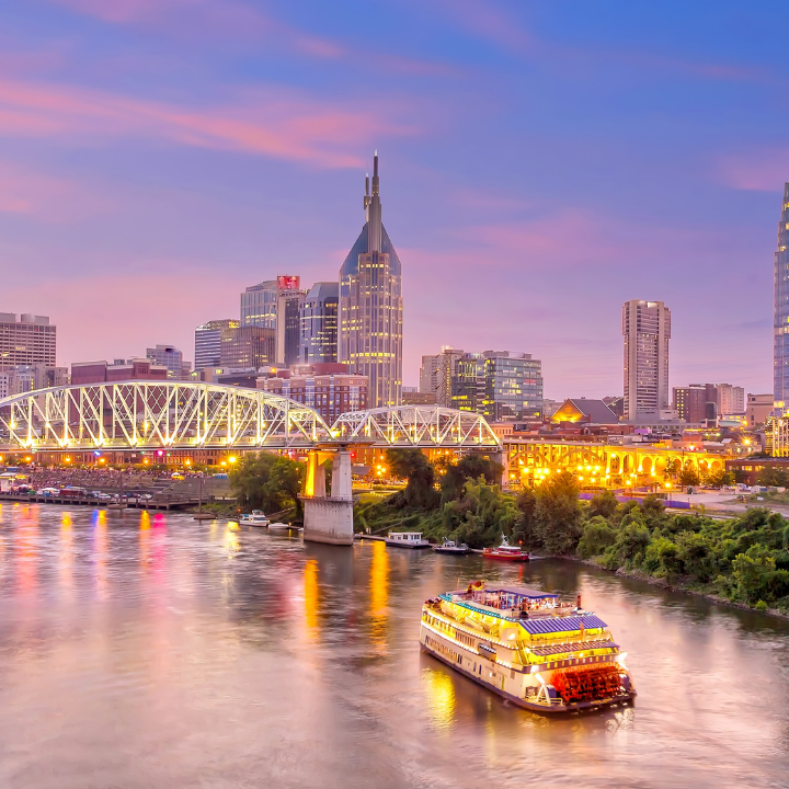 Downtown Nashville skyline at sunset with the John Seigenthaler Pedestrian Bridge and a riverboat on the Cumberland River.