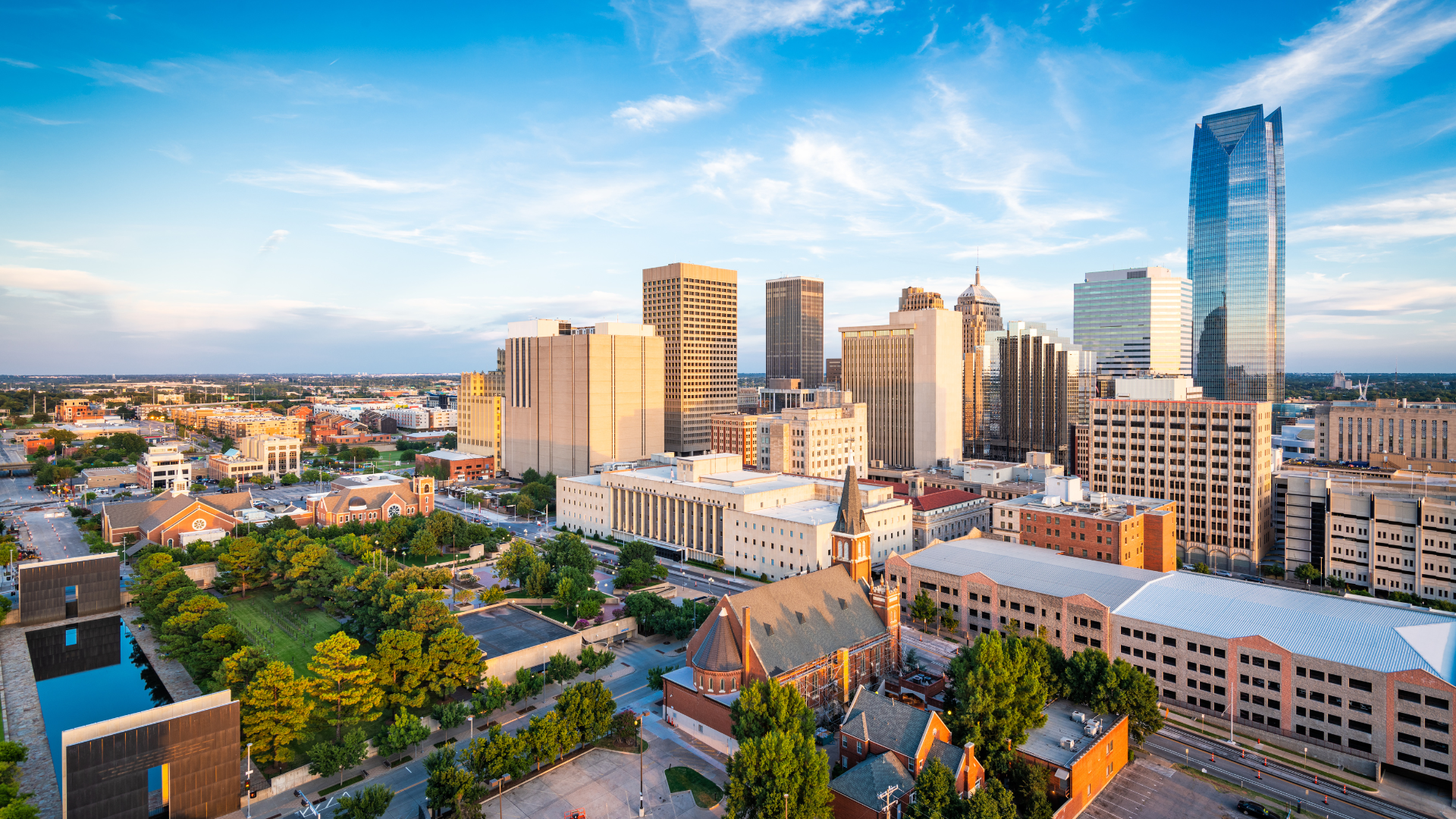 Downtown Oklahoma City skyline with modern high-rise buildings, parks, and historic architecture at sunset