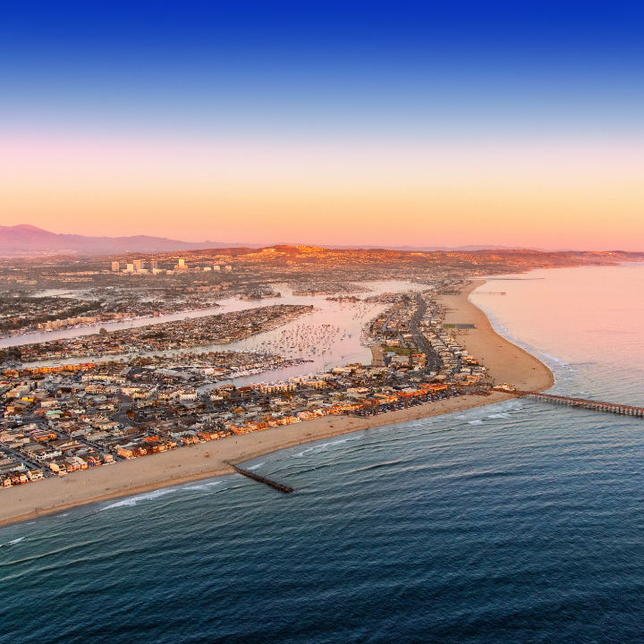 Aerial view of Orange County, CA at sunset with a long stretch of beach, marina-filled harbors, and a coastal community nestled between the ocean and hills—representing the region served by temp staffing and consulting experts.