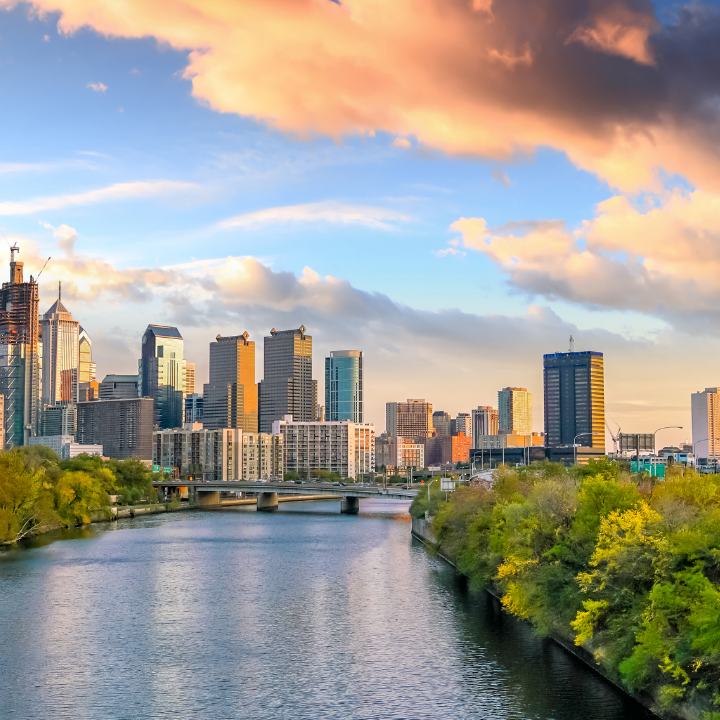 A glowing sunset over downtown Philadelphia, with the Schuylkill River in the foreground and a mix of modern skyscrapers and lush greenery—representing the city’s role in leading temp staffing and consulting.