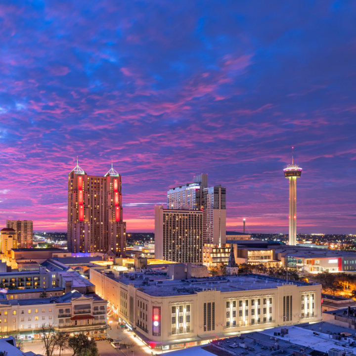 San Antonio skyline at sunset featuring the Tower of the Americas and downtown buildings under a colorful sky.