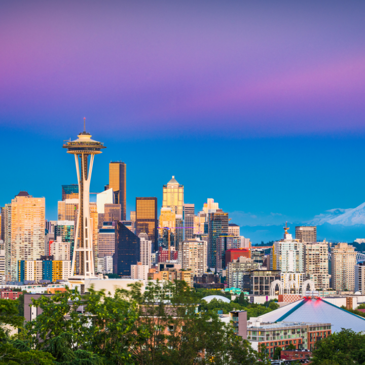 Seattle skyline at dusk with the Space Needle and Mount Rainier in the background under a vibrant sky.