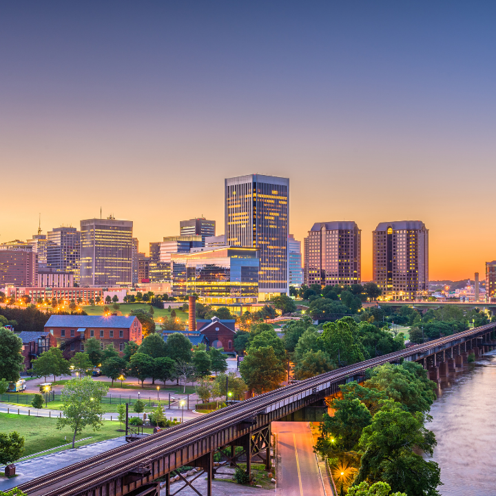 Skyline of downtown Richmond, Virginia, at dusk with city lights and train tracks in the foreground.